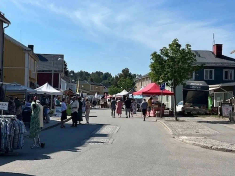 Vy över en gågata under vårmarknad med hus och marknadsstånd och besökare