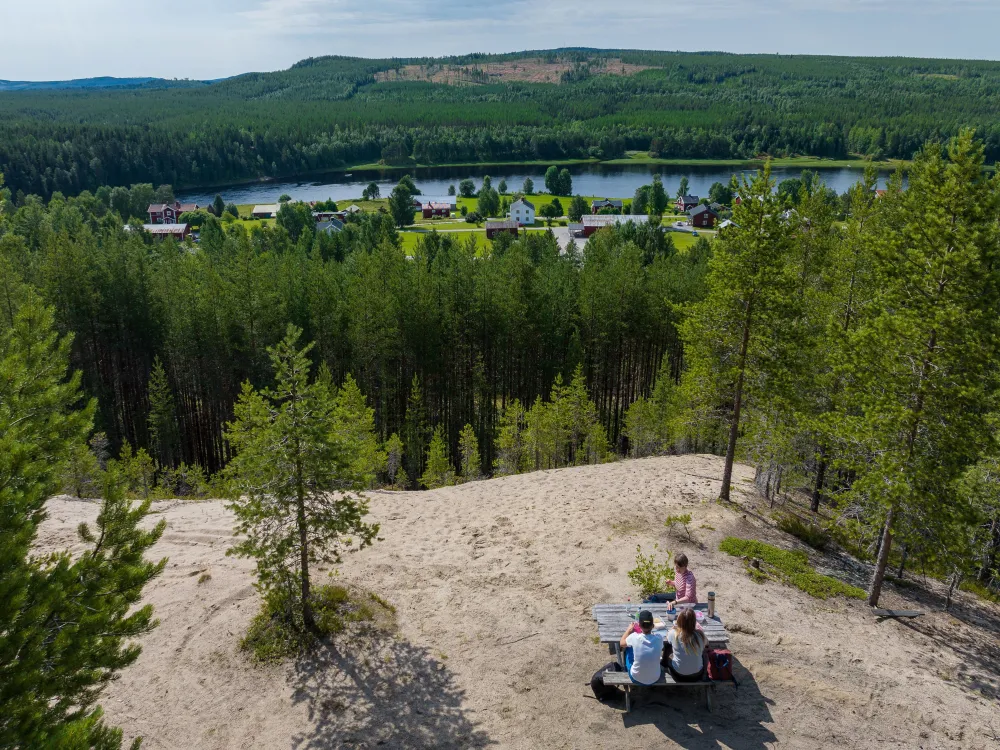 tre vandrare som fikar i naturen på en rastplats med utsikt över älv och skog