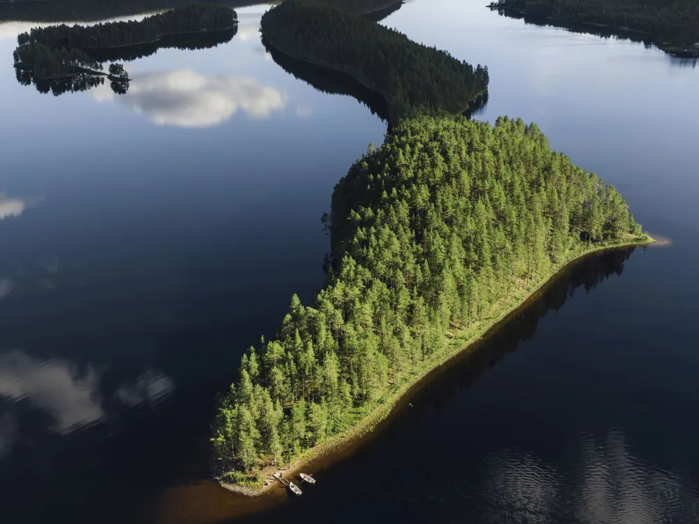 skogsbeklädd smal halvö fotad ovanifrån en stilla dag med blank sjö
