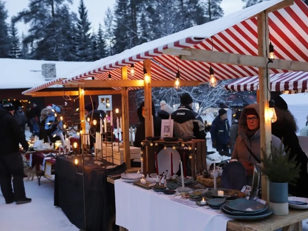 Outdoor Christmas market in the snow with red-and-white striped stalls.