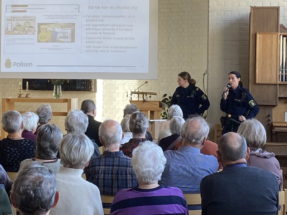 två kvinnliga poliser föreläser inför pensionärer i en stor sal