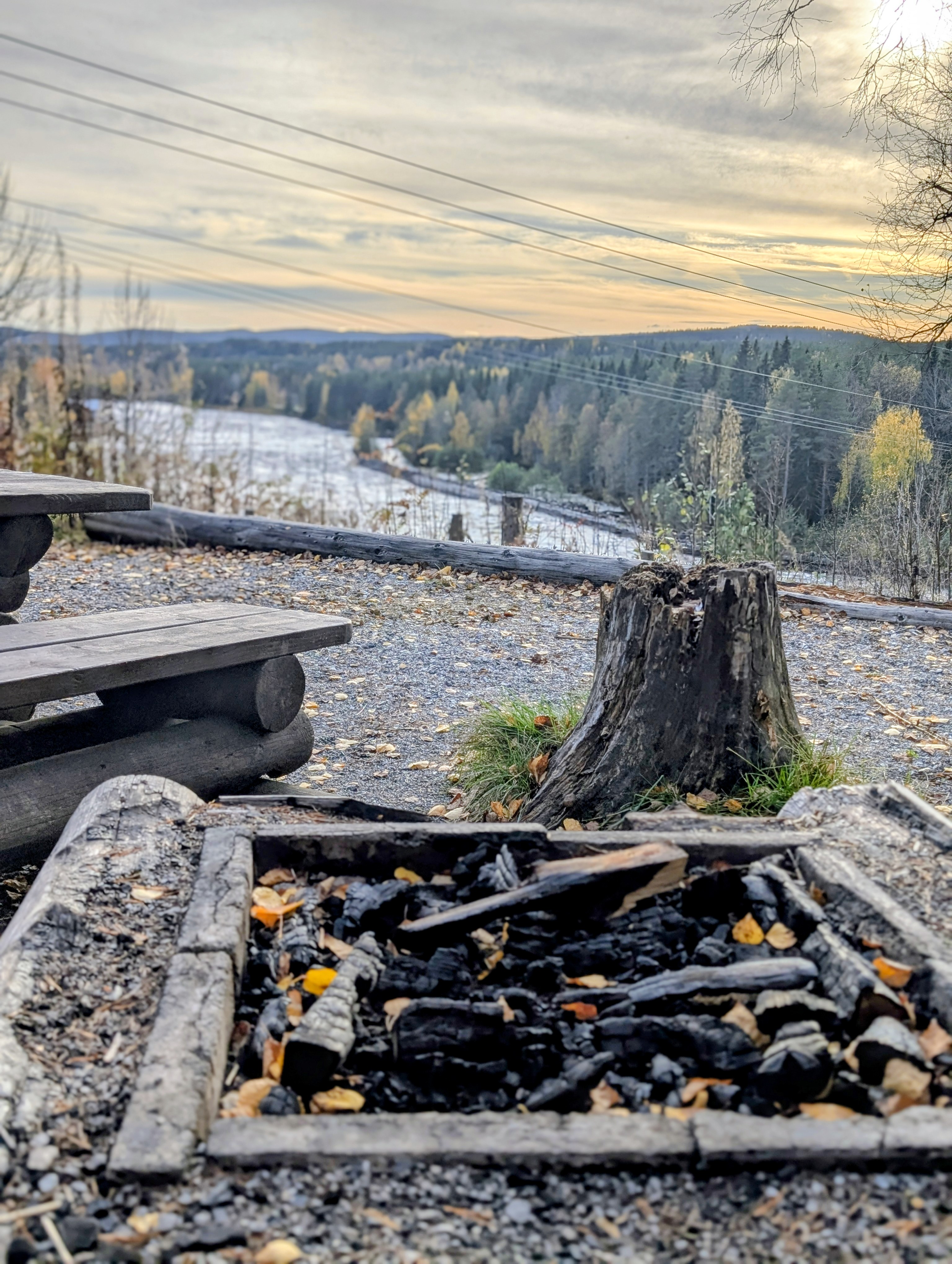 Grillplats med eldstad och träbänk ovanför Renforsen, med Vindelälven i bakgrunden.