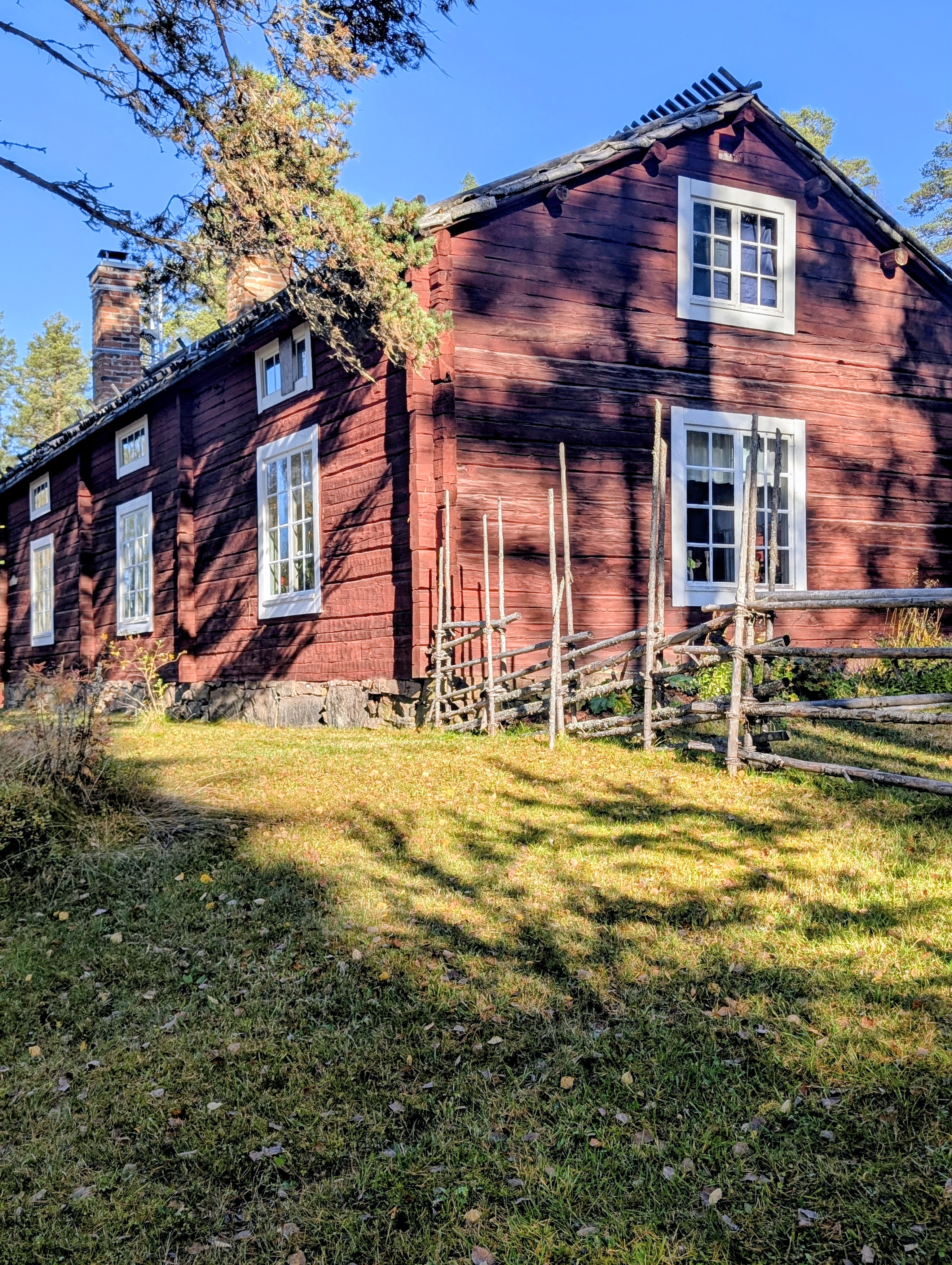Röd timmerbyggnad med vita fönster och gärdesgård på Vindelns hembygdsgård.